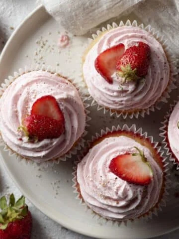 Homemade strawberry cupcakes recipe with pink frosting and sliced strawberries on a white kitchen counter in natural light.