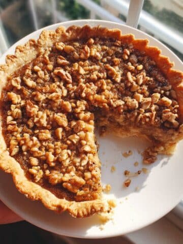 A top-down shot of a homemade walnut maple pie with a golden crust and visible toasted walnuts on a white kitchen table.