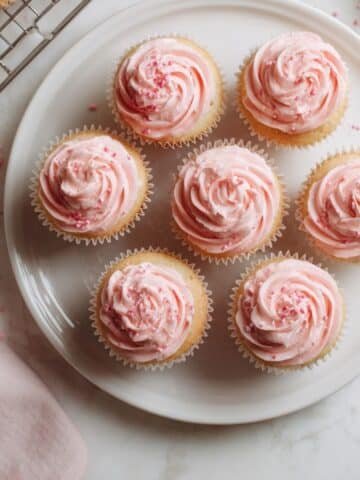 Homemade pink cupcakes with fluffy frosting on a white kitchen table.