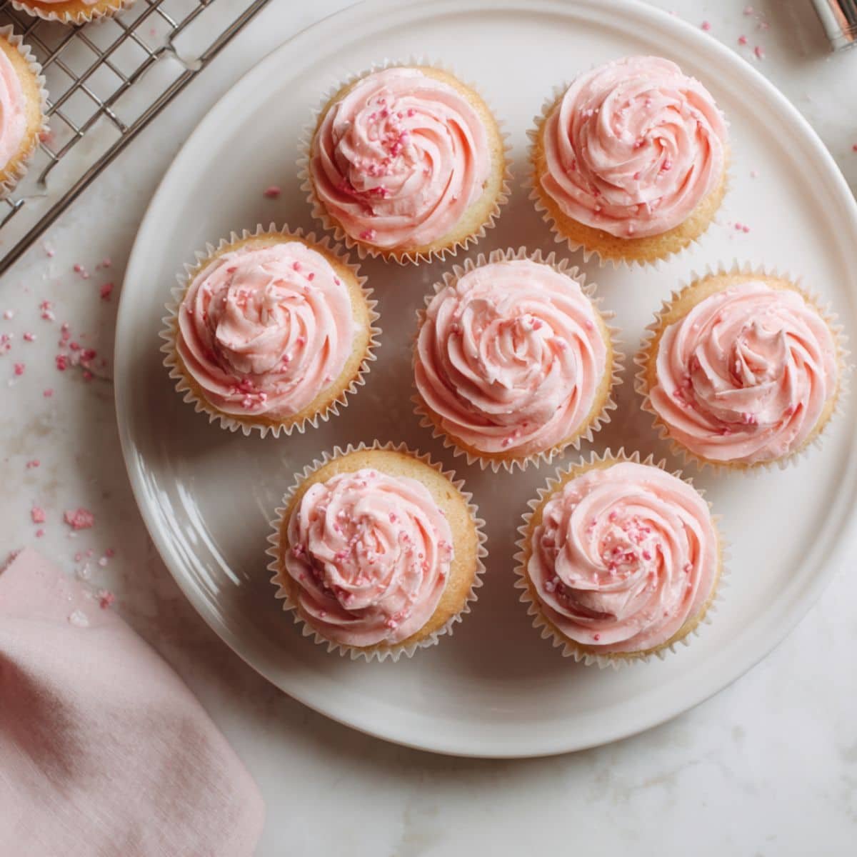 Homemade pink cupcakes with fluffy frosting on a white kitchen table.