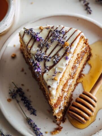 Rustic homemade honey lavender cake slice with creamy lavender frosting and honey drizzle on a white kitchen table, shot from above in natural light.