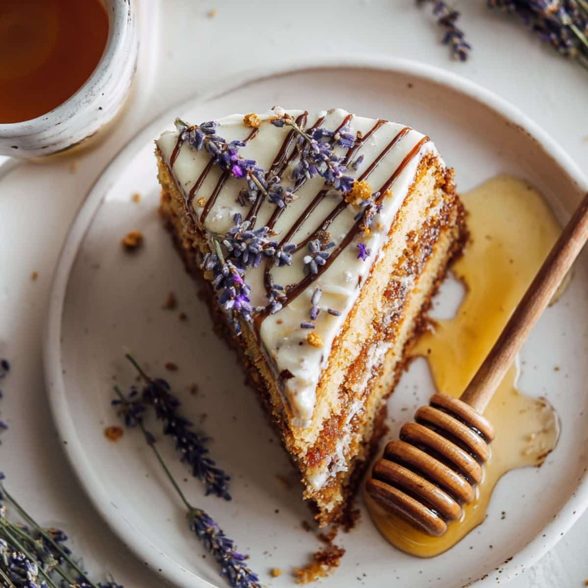 Rustic homemade honey lavender cake slice with creamy lavender frosting and honey drizzle on a white kitchen table, shot from above in natural light.