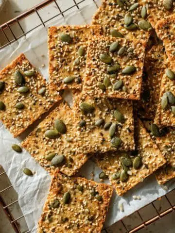 Homemade keto crackers recipe cooling on a wire rack in natural light on a white kitchen table.