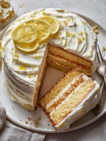 A slice of homemade lemon pie cake with creamy lemon filling and whipped frosting on a white kitchen table, photographed from above.