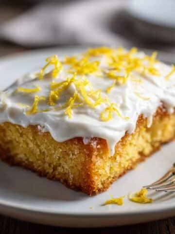 Homemade lemon sheet cake with cream cheese frosting and lemon zest on a white kitchen table, photographed from above.
