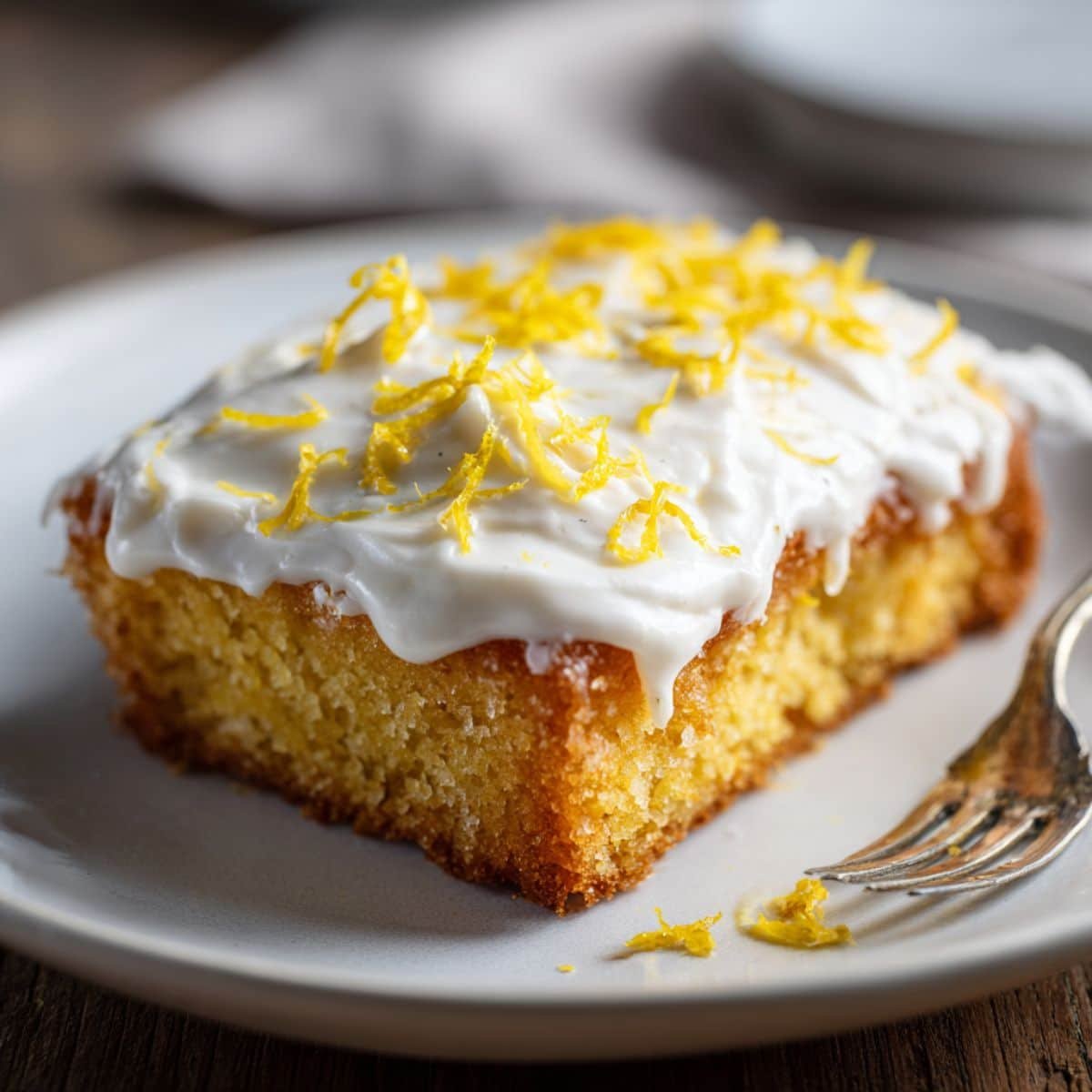 Homemade lemon sheet cake with cream cheese frosting and lemon zest on a white kitchen table, photographed from above.