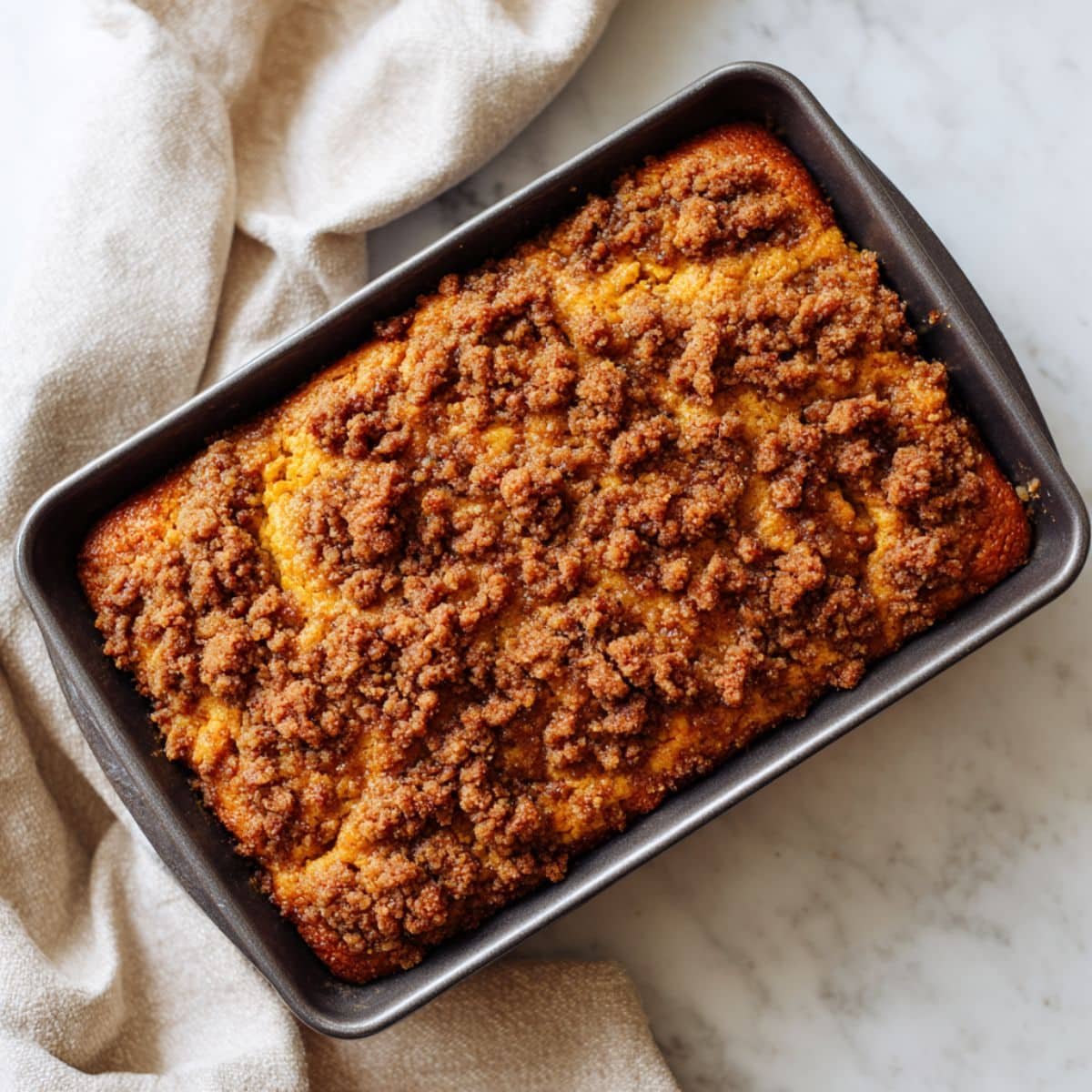 Homemade pumpkin cinnamon coffee cake with streusel topping on a white kitchen table, sliced imperfectly to show moist pumpkin texture.