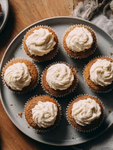 Homemade pumpkin ginger cupcakes with cream cheese frosting on a white table, photographed from above.