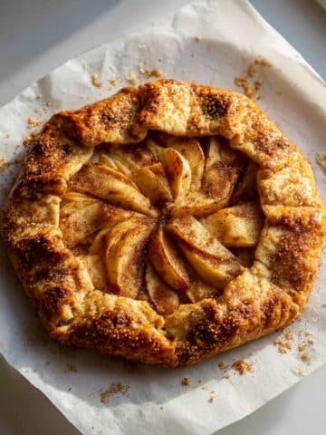 Homemade apple galette puff pastry on a white kitchen table, golden and flaky with rustic folds and cinnamon apples in the center.