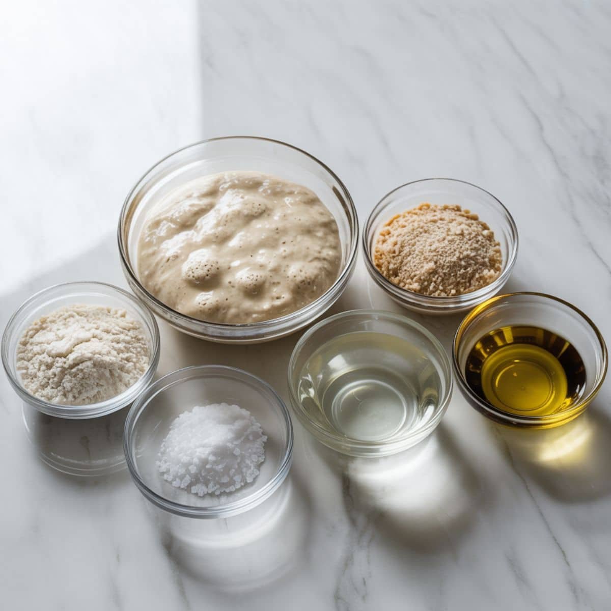 Top-down photo of sourdough tortilla ingredients on a white kitchen counter — flour, sourdough starter, water, salt, and olive oil.