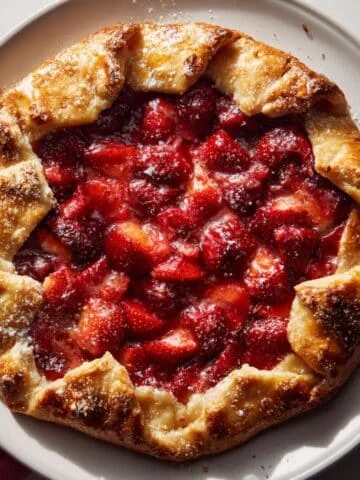 Homemade strawberry crostata with golden crust and jammy strawberry filling on a white kitchen table, photographed from above in natural light.