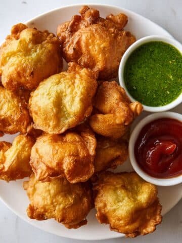 Golden crispy bread pakoras recipe on a white plate with chutney and ketchup, photographed top-down on a white kitchen table in a real homemade setting