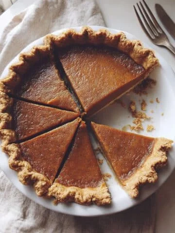 Homemade chai pumpkin pie sliced on a white kitchen table, shot from above with natural lighting.