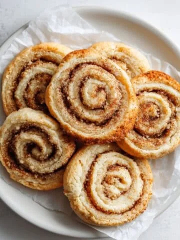 Homemade cinnamon roll sugar cookies with golden swirls cooling on a white counter.