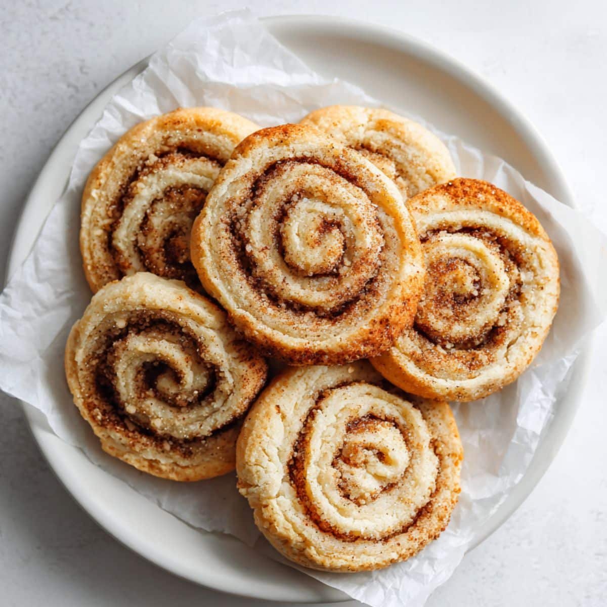 Homemade cinnamon roll sugar cookies with golden swirls cooling on a white counter.