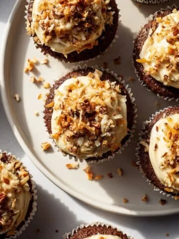 Homemade German chocolate cupcakes with coconut pecan frosting on a white table.