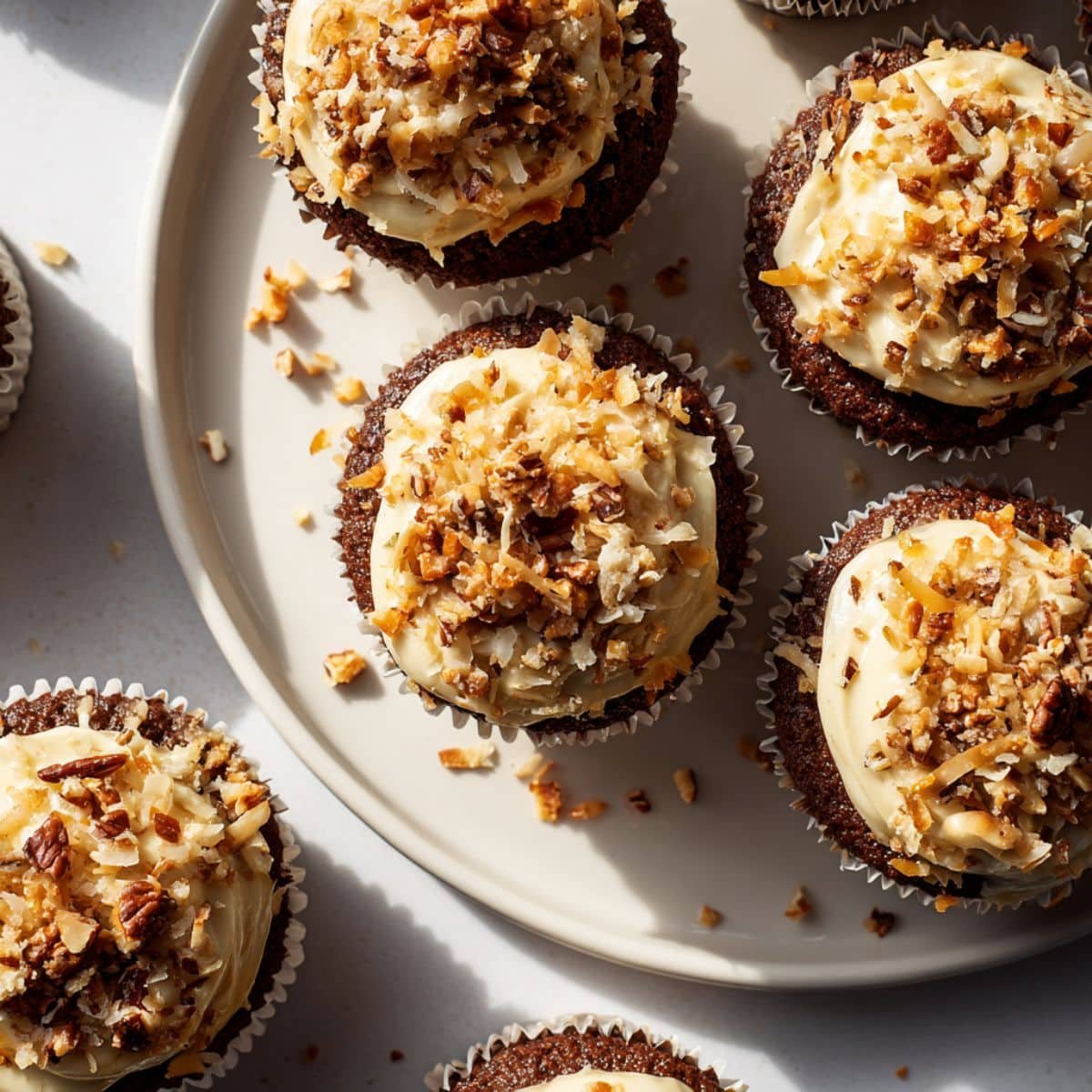 Homemade German chocolate cupcakes with coconut pecan frosting on a white table.