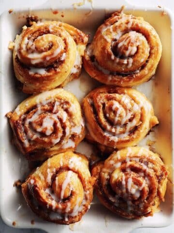 Golden brown puff pastry cinnamon rolls drizzled with glaze on a white kitchen counter, shot from above in natural light.