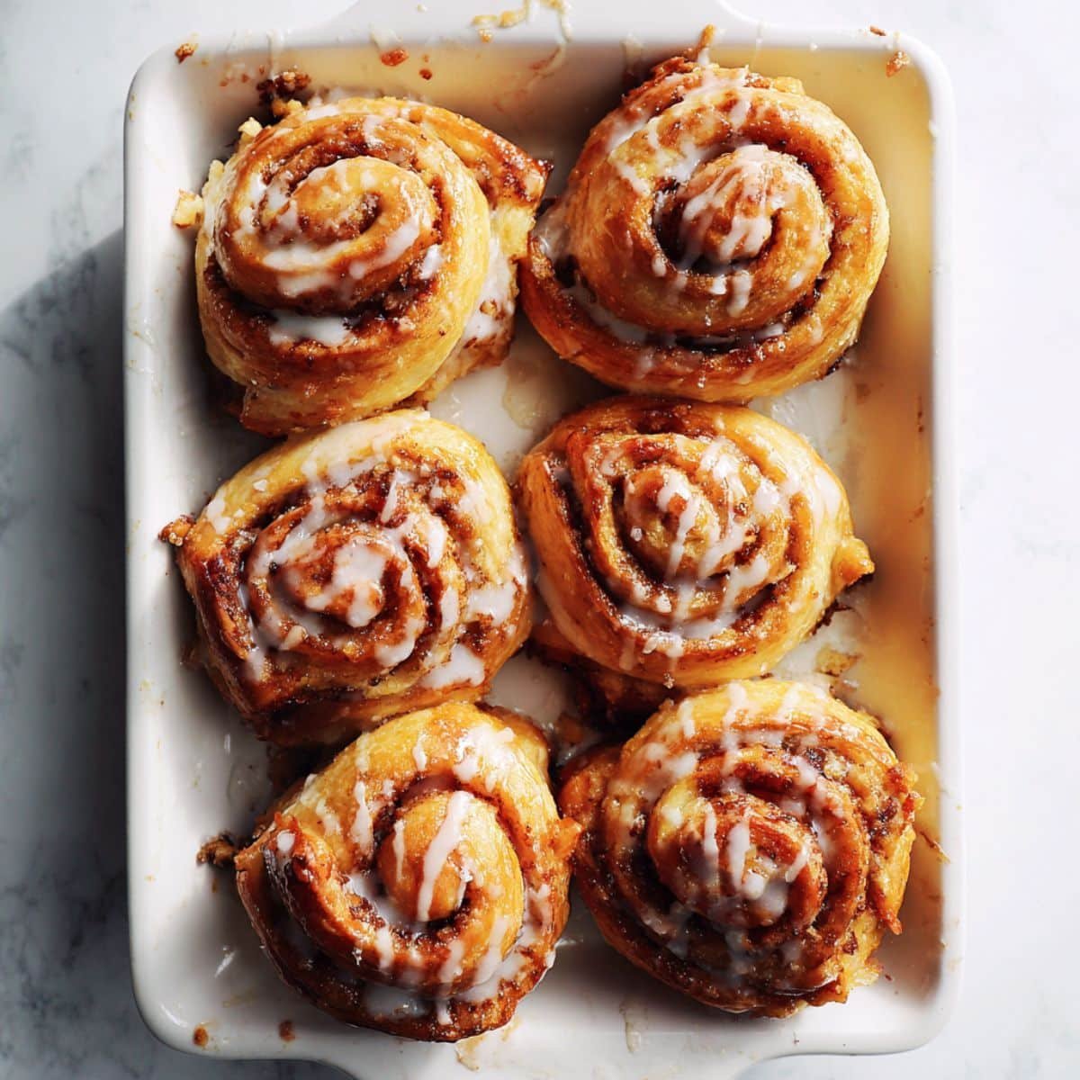 Golden brown Cinnamon Rolls Puff Pastry drizzled with glaze on a white kitchen counter, shot from above in natural light.