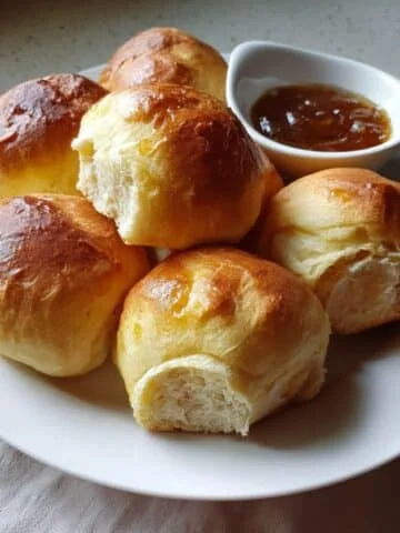 Soft golden Texas Roadhouse Rolls brushed with butter, served with cinnamon honey butter on a white kitchen counter.