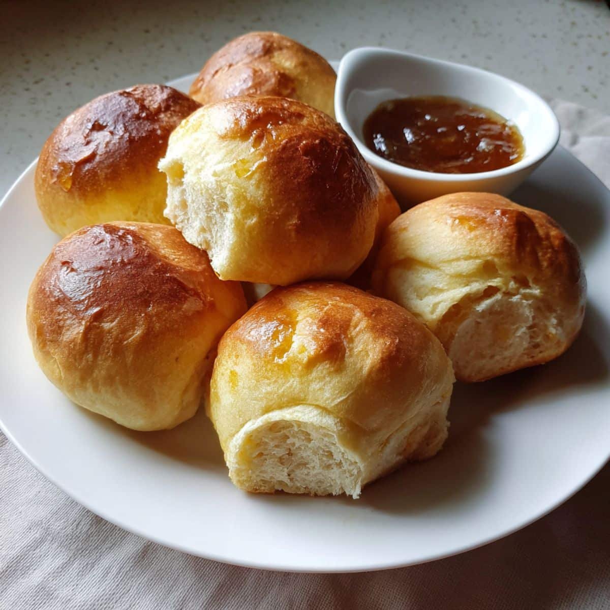 Soft golden Texas Roadhouse Rolls brushed with butter, served with cinnamon honey butter on a white kitchen counter.