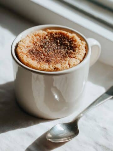 A homemade almond flour mug cake in a white mug on a kitchen table, photographed from above in natural light.