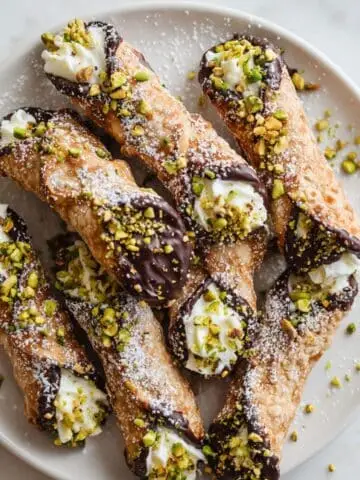 Top-down view of homemade chocolate dipped cannoli with pistachio garnish on a white kitchen table