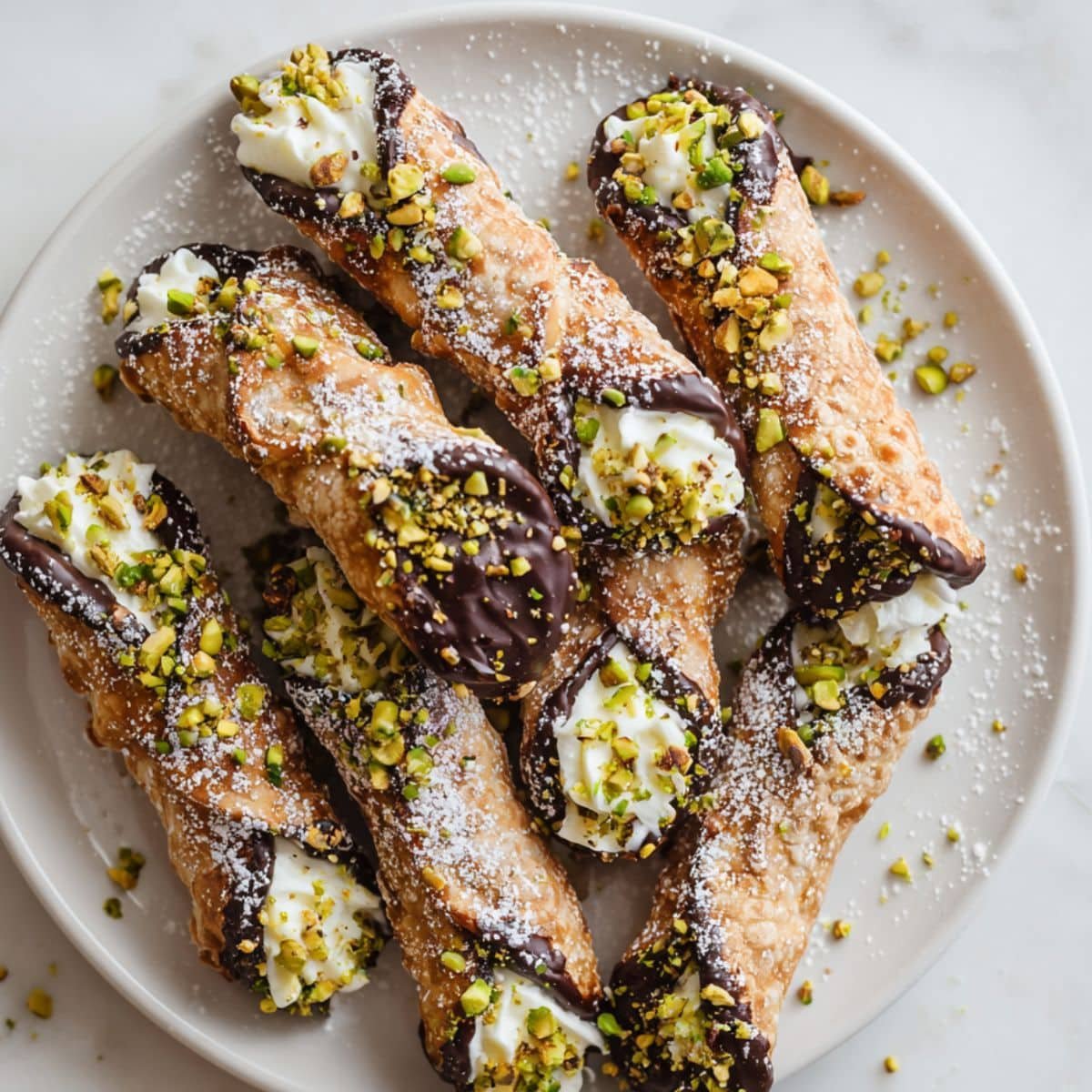 Top-down view of homemade chocolate dipped cannoli with pistachio garnish on a white kitchen table