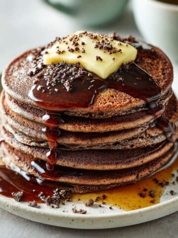 A stack of fluffy homemade chocolate pancakes with syrup on a white kitchen table, photographed from above in natural light.