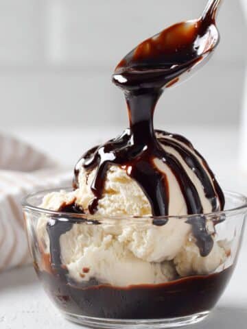 Homemade hot fudge sauce drizzled over vanilla ice cream on a white kitchen counter.