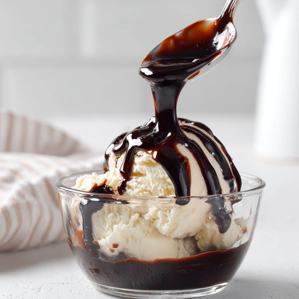 Homemade hot fudge sauce drizzled over vanilla ice cream on a white kitchen counter.