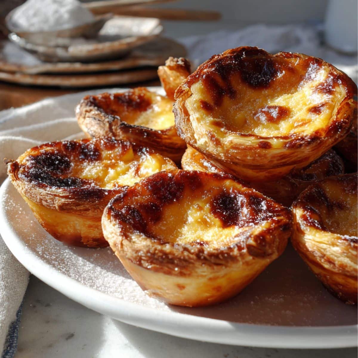 Freshly baked Portuguese custard tarts with golden caramelized tops cooling on a white kitchen table, photographed from above in natural light.