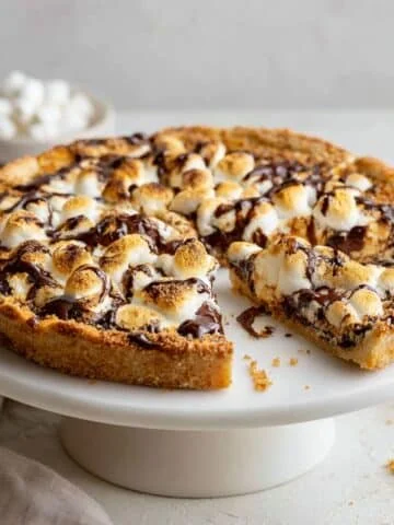 Homemade s’mores pizza topped with melted chocolate and toasted marshmallows on a white kitchen counter