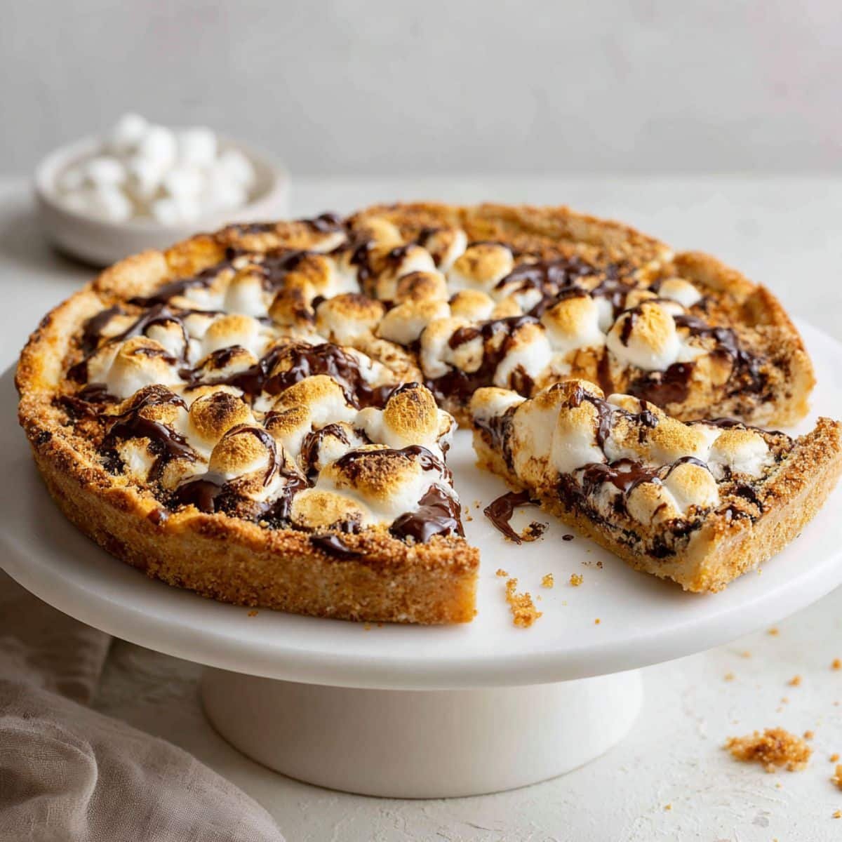Homemade s’mores pizza topped with melted chocolate and toasted marshmallows on a white kitchen counter