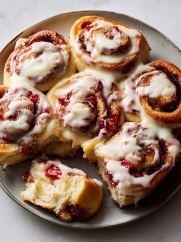 Freshly baked strawberry cinnamon rolls with cream cheese frosting and strawberry filling on a white kitchen counter, photographed from above in natural light.