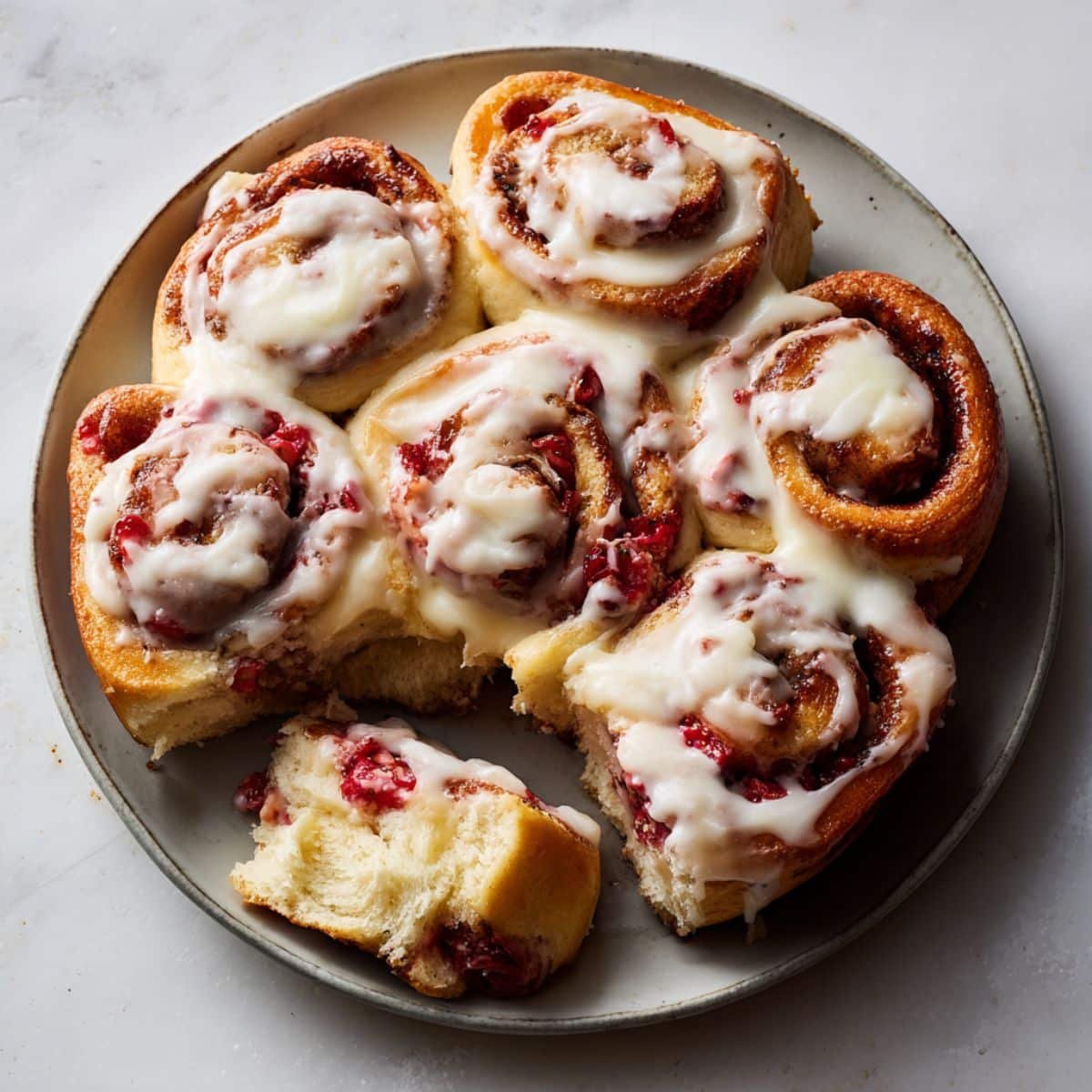 Freshly baked strawberry cinnamon rolls with cream cheese frosting and strawberry filling on a white kitchen counter, photographed from above in natural light.