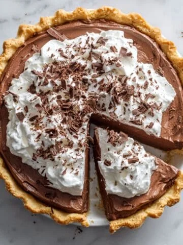 Homemade French silk chocolate pie topped with whipped cream and chocolate shavings on a white kitchen counter, shot from above.