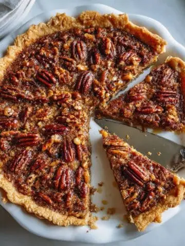 A homemade gluten-free pecan pie with a golden crust and glossy pecan topping cooling on a white kitchen table.