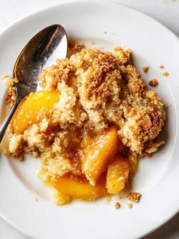 Freshly baked keto peach cobbler with golden almond flour crust on a white kitchen table