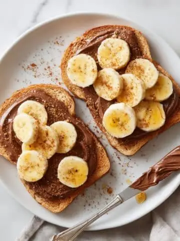 Homemade Nutella and banana toast on a white kitchen table with fresh banana slices and honey drizzle, photographed from above.