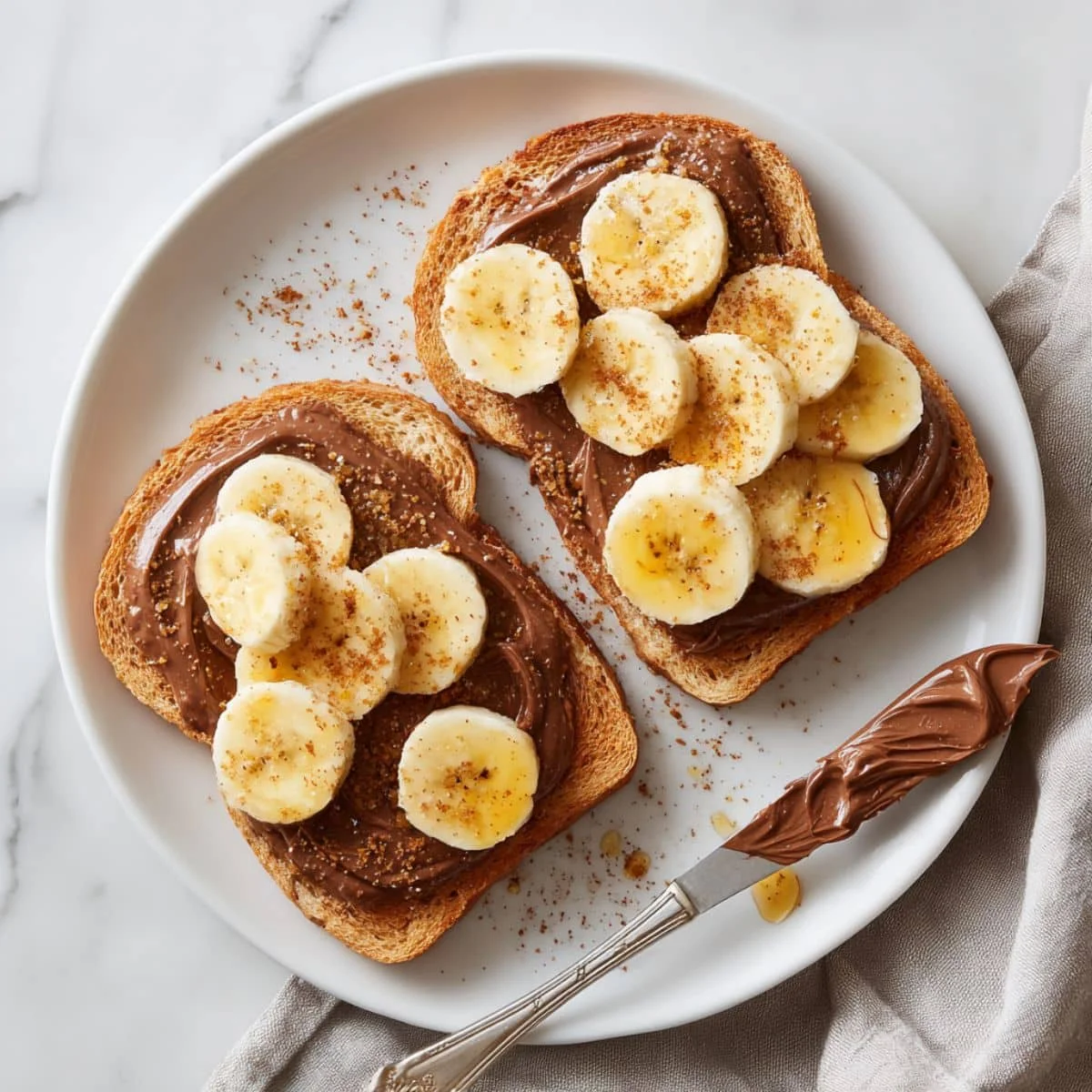Homemade Nutella and banana toast on a white kitchen table with fresh banana slices and honey drizzle, photographed from above.
