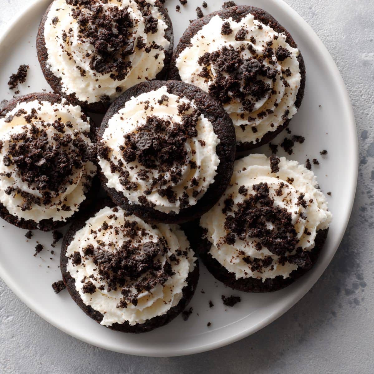Homemade Oreo Crumbl cookie topped with cream cheese frosting and crushed Oreos on a white kitchen counter.