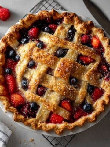 Homemade three berry pie with golden crust and juicy filling cooling on a white kitchen counter.