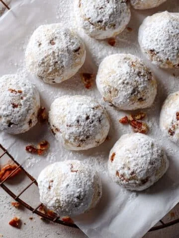 Homemade vegan Mexican wedding cookies dusted with powdered sugar on a white kitchen table.