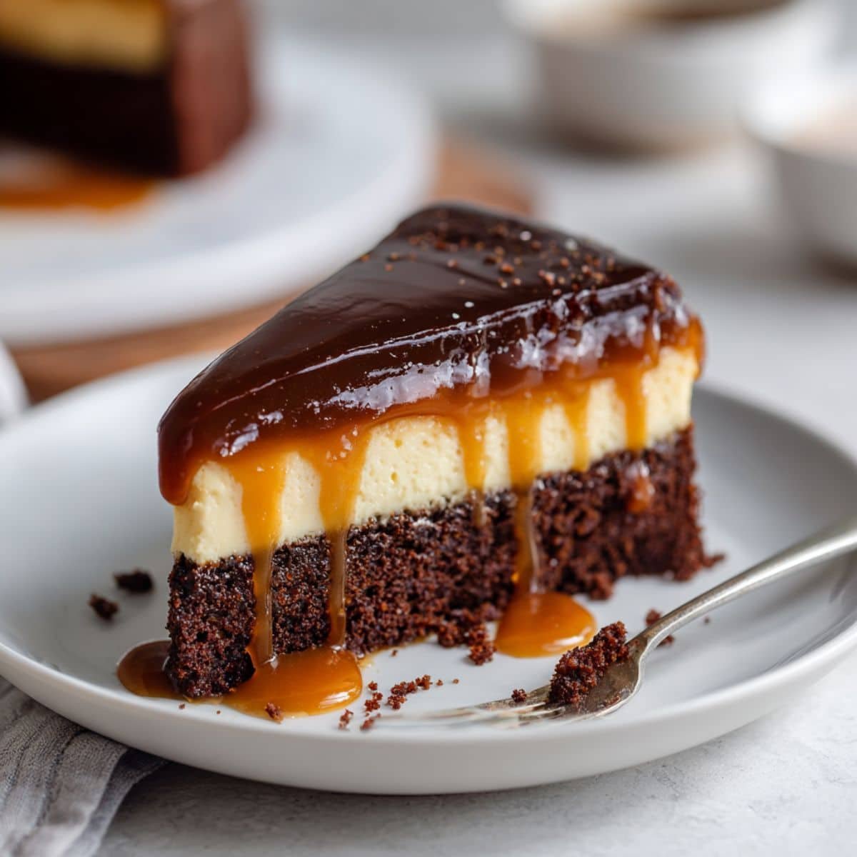 Homemade chocolate flan cake slice with caramel sauce dripping over the layers on a white plate, shot from above on a white counter
