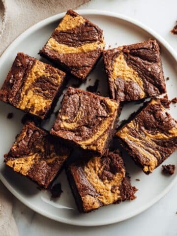Homemade peanut butter brownies with chocolate swirl on a white plate, photographed from above on a white kitchen counter.