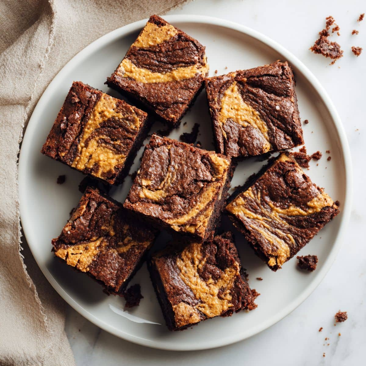 Homemade peanut butter brownies with chocolate swirl on a white plate, photographed from above on a white kitchen counter.