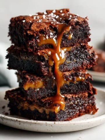Stack of gooey chocolate caramel brownies with caramel drizzle on a white plate, top-down homemade shot.