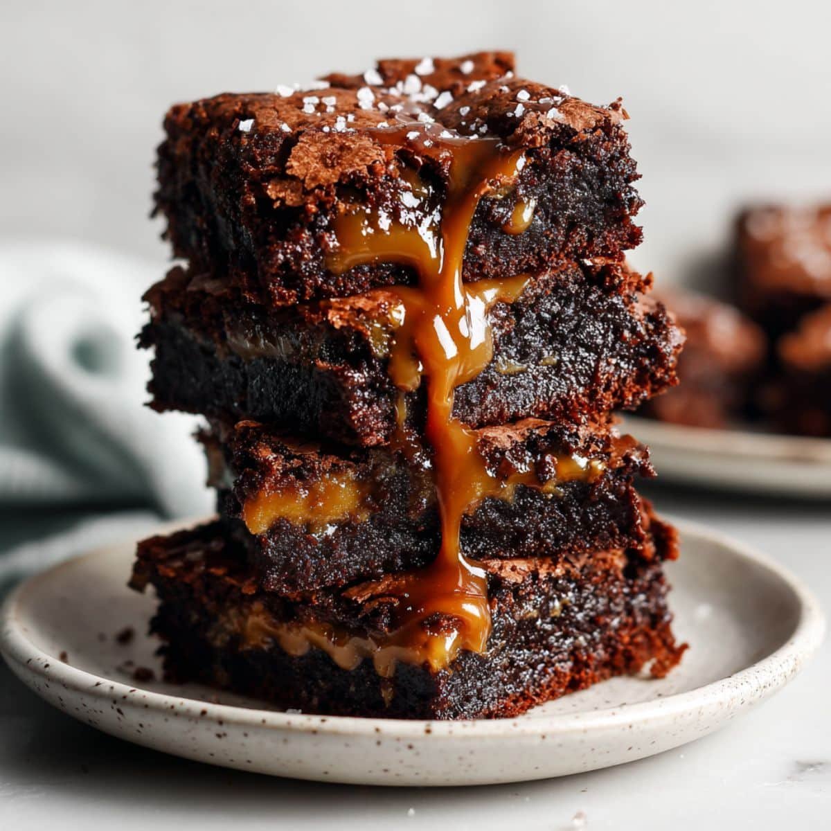 Stack of gooey chocolate caramel brownies with caramel drizzle on a white plate, top-down homemade shot.