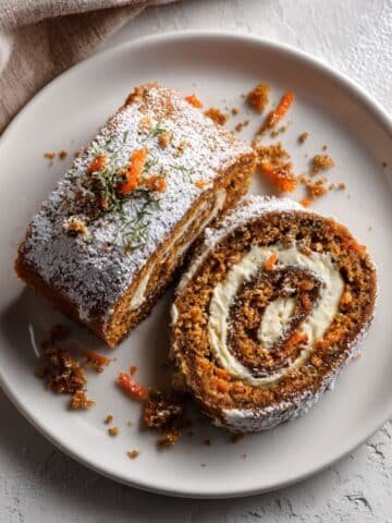 Homemade carrot cake roll slice with cream cheese filling on a white plate, photographed from above in natural light.